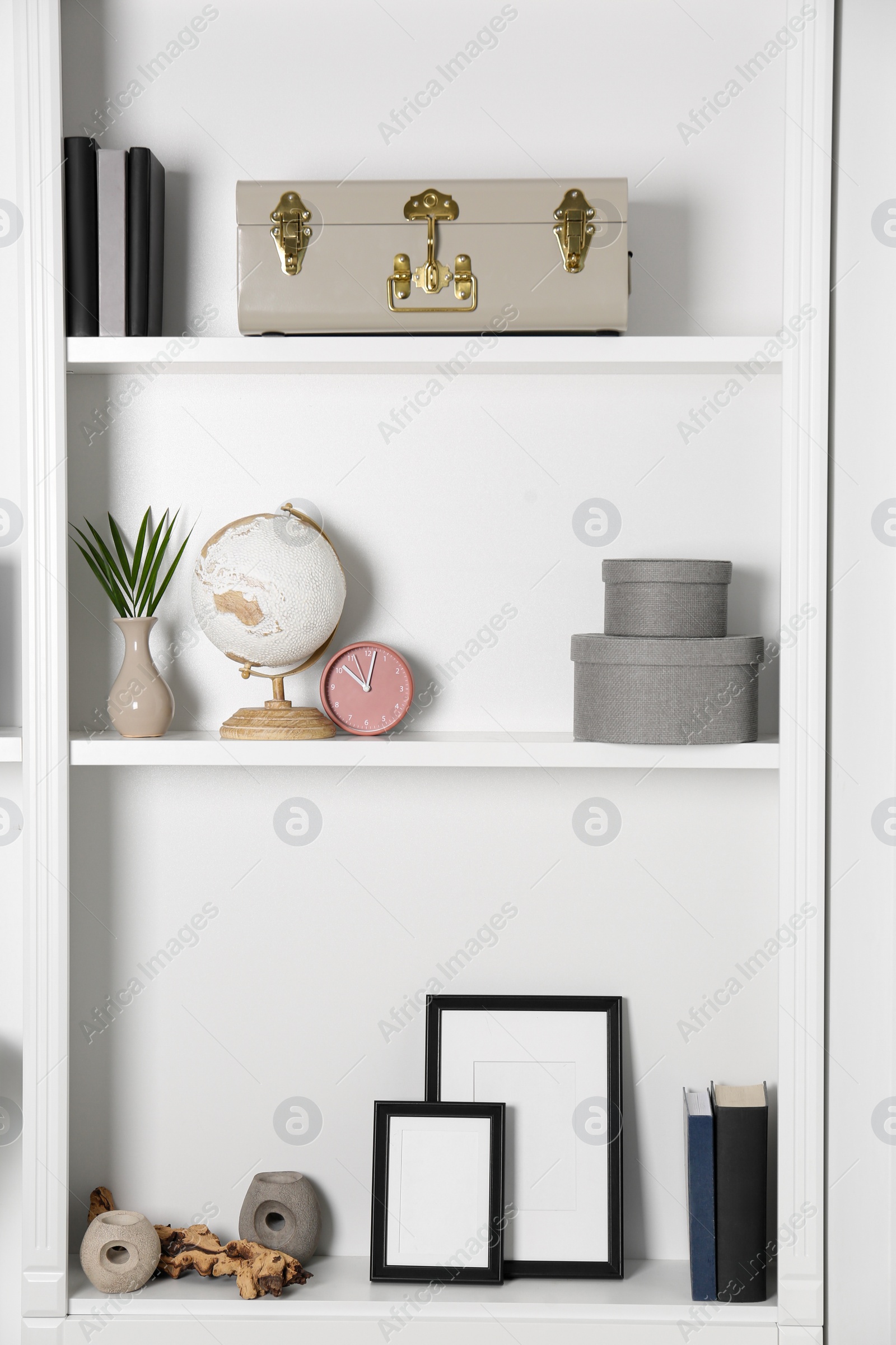 Photo of White shelves with globe, clock and different decor indoors. Interior design