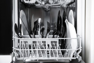 Photo of Open dishwasher with dirty tableware in kitchen, closeup