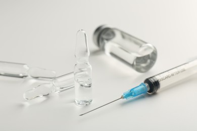 Photo of Glass ampoules with liquid and syringe on white background, closeup