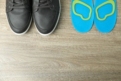 Photo of Orthopedic insoles near shoes on floor, flat lay. Space for text