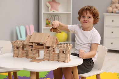Photo of Little boy playing with wooden entry gate and car at white table in room. Child's toys