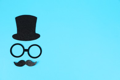 Photo of Man's face made of fake mustache, hat and glasses on light blue background, top view. Space for text