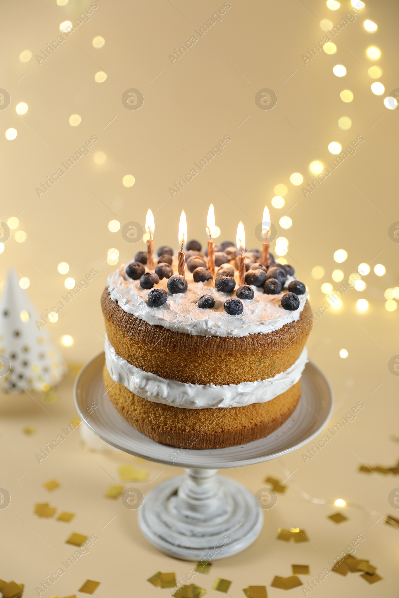 Photo of Tasty cake with burning candles on beige background against blurred lights