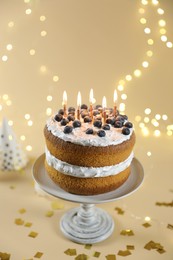 Photo of Tasty cake with burning candles on beige background against blurred lights