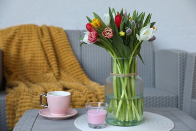 Beautiful bouquet of colorful tulips, cup with drink and candle on rattan garden table