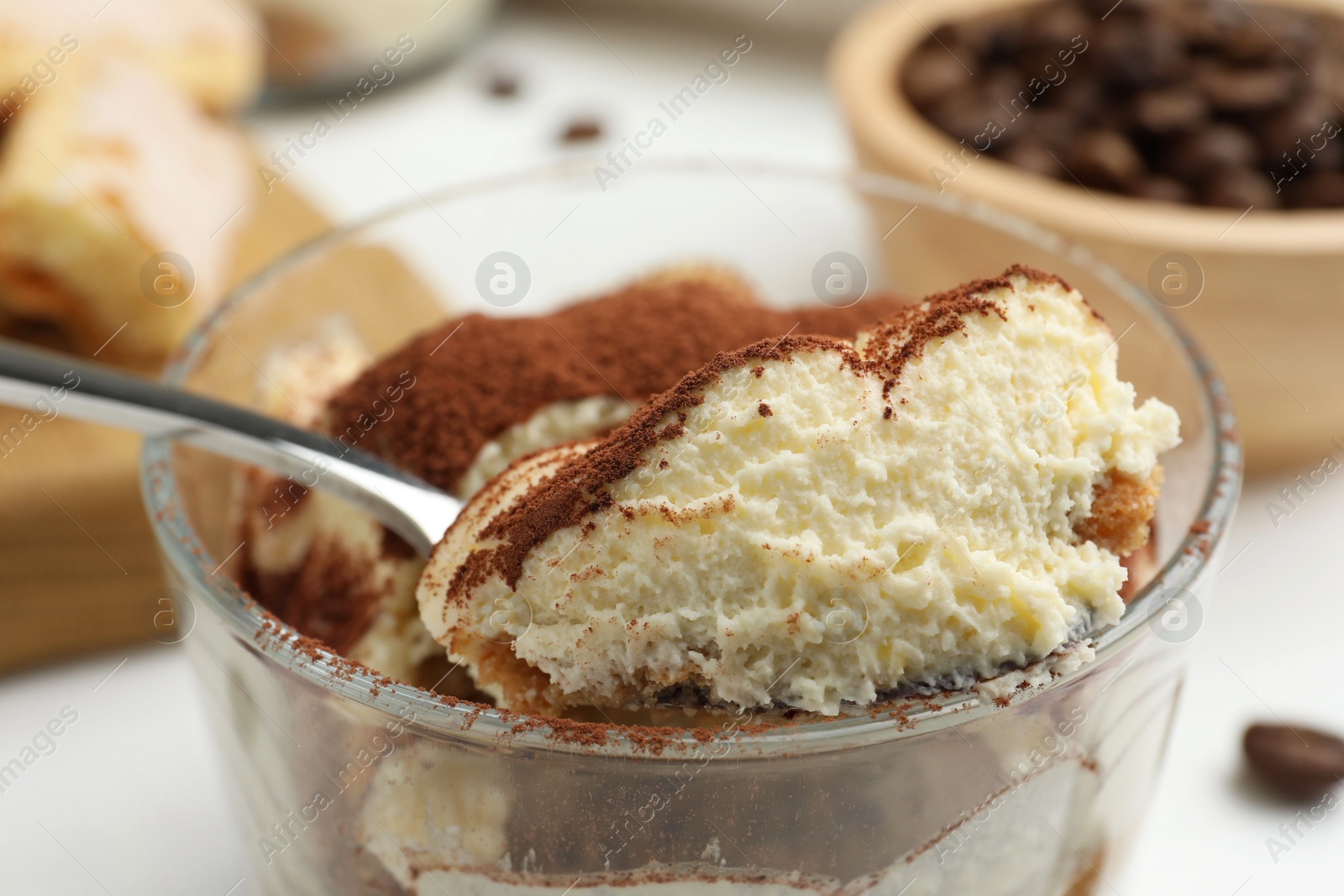 Photo of Delicious tiramisu in glass and spoon on table, closeup