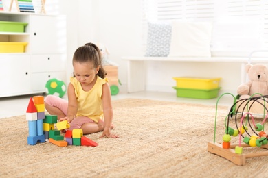 Photo of Cute little girl playing with colorful blocks on floor indoors, space for text. Educational toy