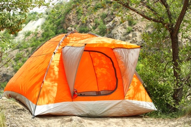 Modern camping tent near tree in wilderness