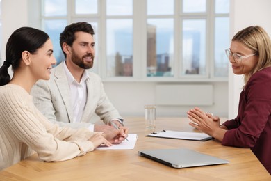 Real estate agent and couple signing contract at table in new apartment