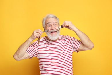 Photo of Senior man with mustache holding blade and brush on orange background