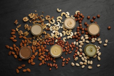 Photo of Different types of delicious nut butters and ingredients on black table, flat lay