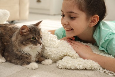 Cute little girl with cat lying on carpet at home. First pet