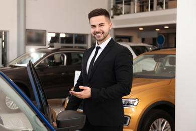 Photo of Young salesman near new car in dealership