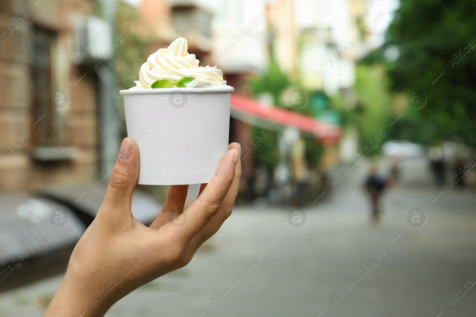 Photo of Woman holding cup with tasty frozen yogurt outdoors, closeup. Space for text