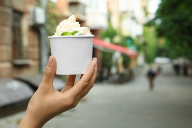 Woman holding cup with tasty frozen yogurt outdoors, closeup. Space for text