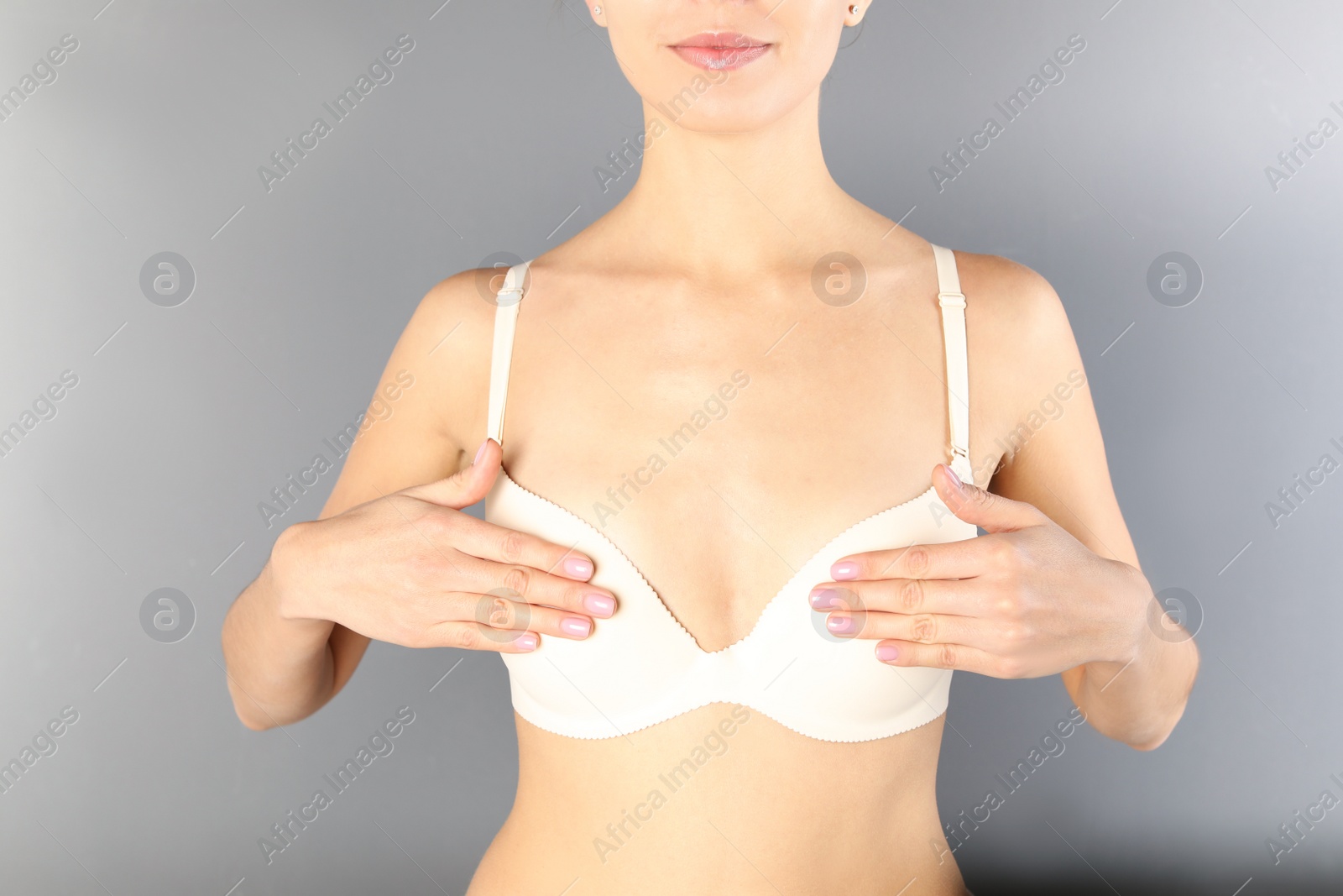 Photo of Young woman in white bra on gray background, closeup. Breast cosmetic surgery