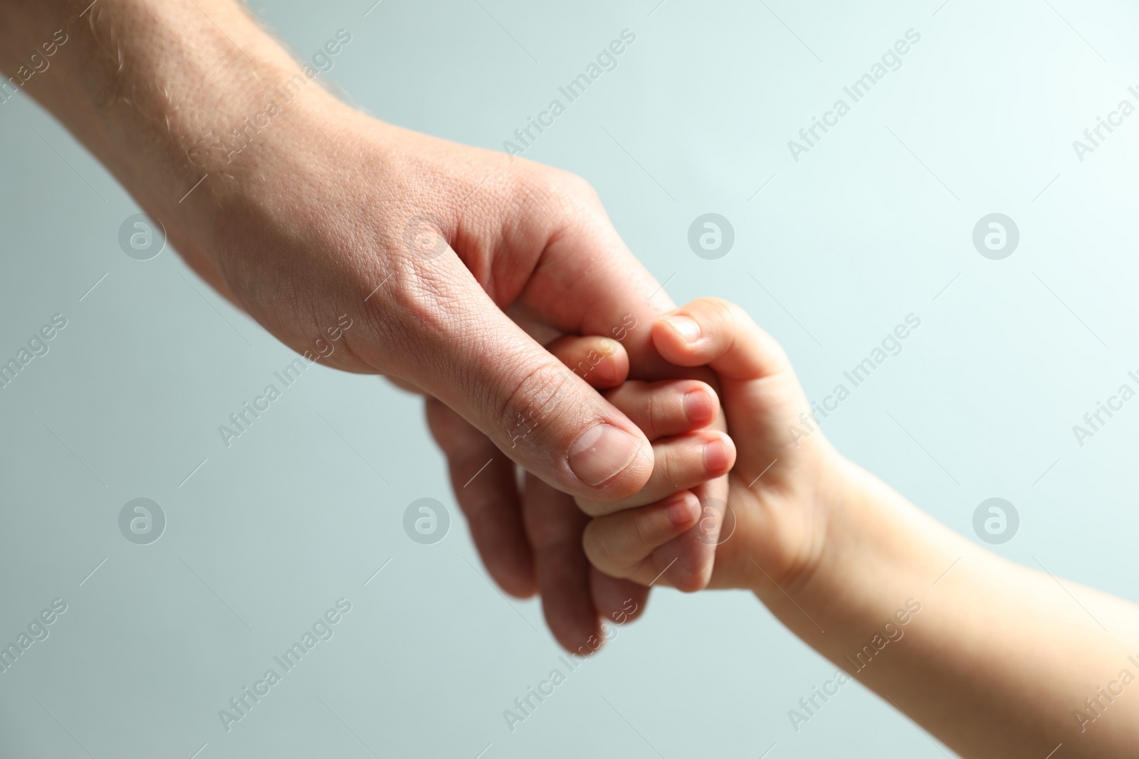 Photo of Father and child holding hands on light blue background, closeup