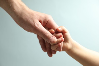 Photo of Father and child holding hands on light blue background, closeup