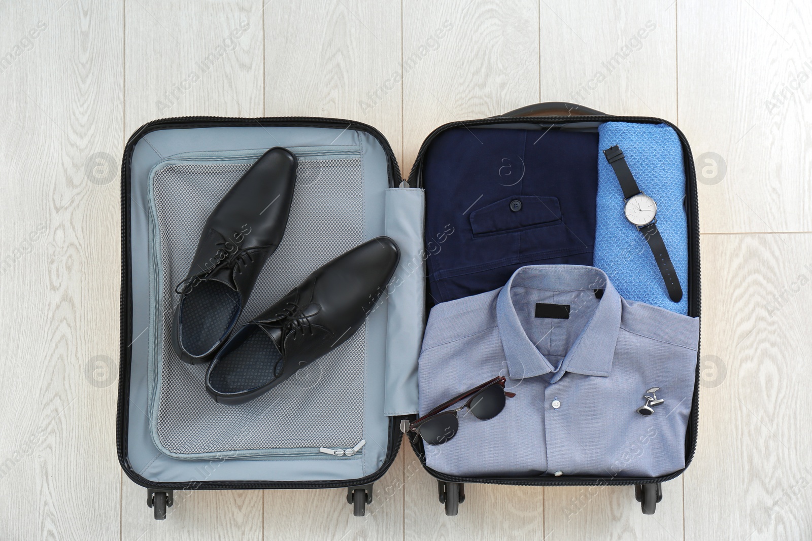 Photo of Open suitcase with clothing, shoes and accessories on wooden background