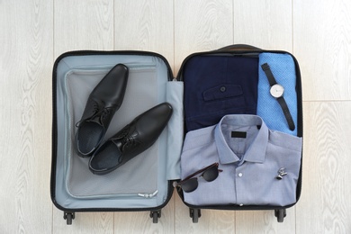 Photo of Open suitcase with clothing, shoes and accessories on wooden background