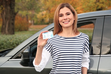 Happy woman holding driving license near car