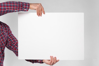 Photo of Man holding sheet of paper on grey background, closeup. Mockup for design