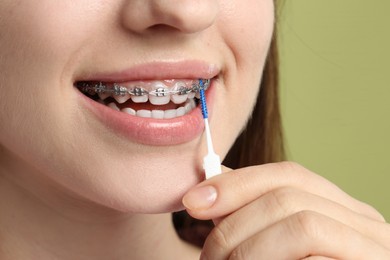 Photo of Smiling woman with dental braces cleaning teeth using interdental brush on light green background, closeup