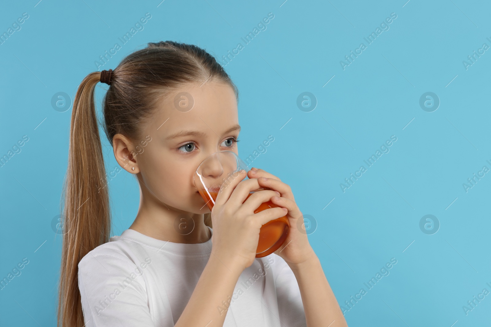 Photo of Little girl drinking fresh juice on light blue background, space for text