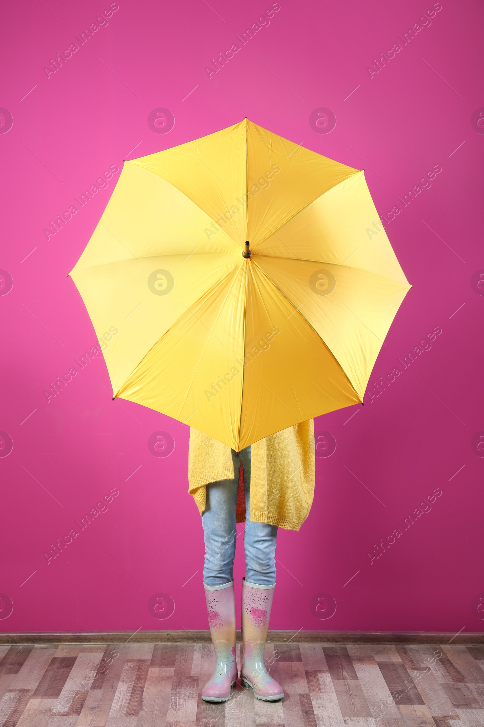 Photo of Woman hiding behind yellow umbrella near color wall