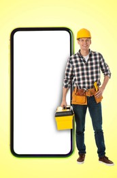 Image of Repair service - just call. Happy professional repairman holding toolbox and smartphone with blank screen on yellow background, space for design
