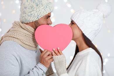 Happy young couple with heart shaped gift box against blurred festive lights. Christmas celebration