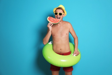 Shirtless man with inflatable ring eating watermelon on color background