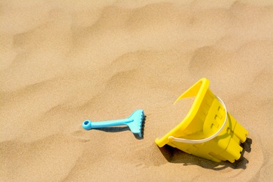 Photo of Plastic bucket and rake on sand, space for text. Beach toys