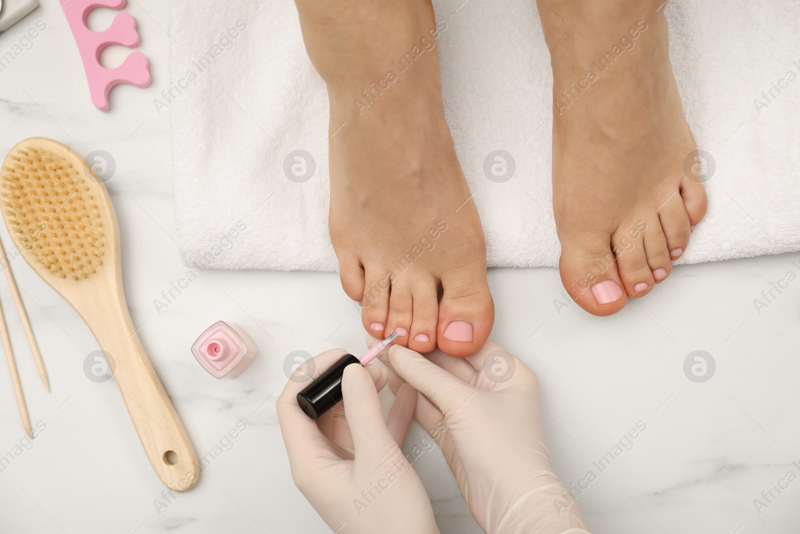 Photo of Professional pedicurist painting client`s toenails with polish in beauty salon, top view