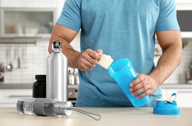 Photo of Man preparing protein shake at wooden table in kitchen, closeup