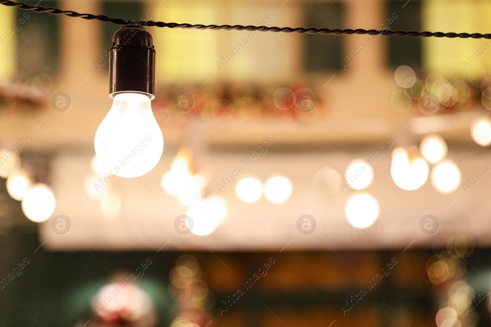 Photo of Glowing bulb on wire against blurred lights. Space for text