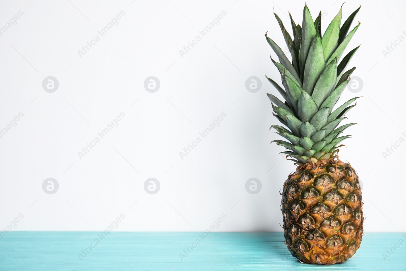 Photo of Fresh ripe juicy pineapple on light blue wooden table. Space for text