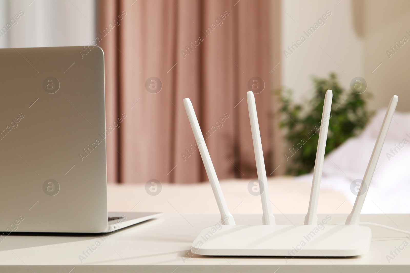 Photo of New Wi-Fi router near laptop on white table indoors