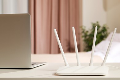 Photo of New Wi-Fi router near laptop on white table indoors