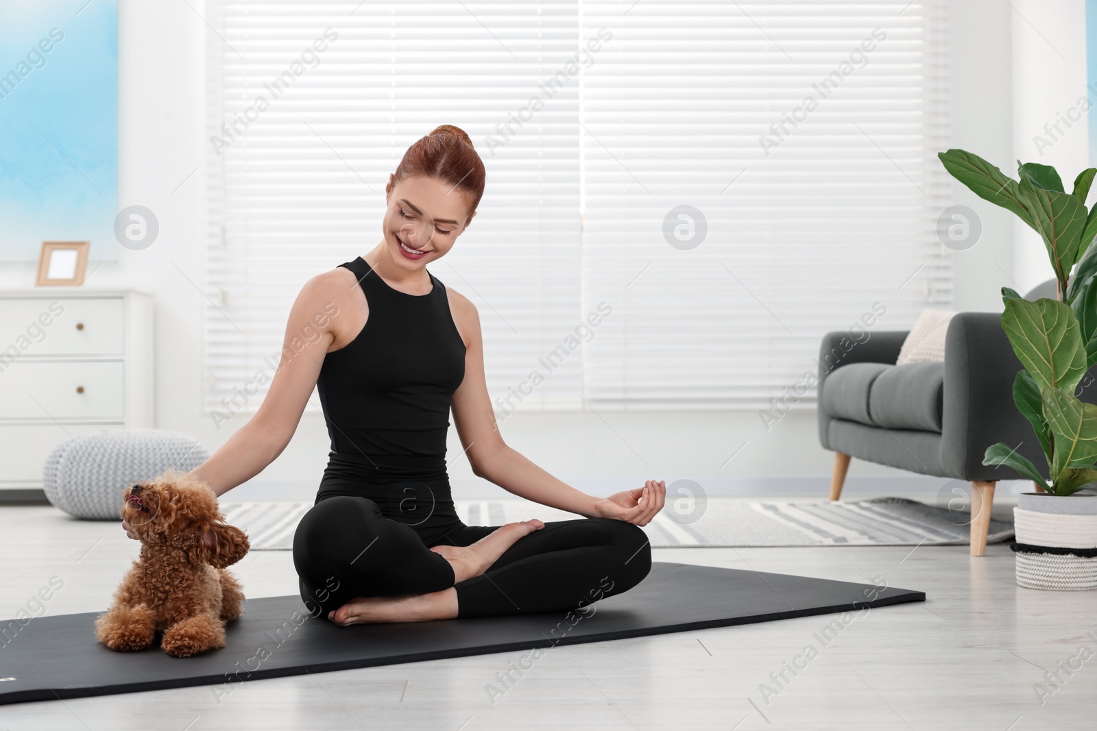 Photo of Happy young woman practicing yoga on mat with her cute dog at home