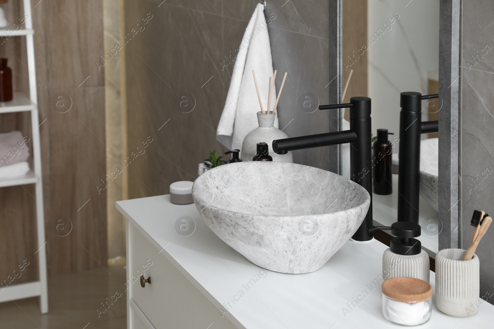 Photo of Stone vessel sink with faucet and toiletries on white countertop in bathroom