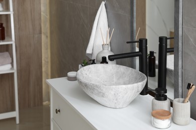 Photo of Stone vessel sink with faucet and toiletries on white countertop in bathroom