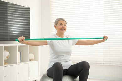 Senior woman doing exercise with elastic resistance band on fitness ball at home