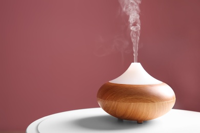 Photo of Aroma oil diffuser on table against color background