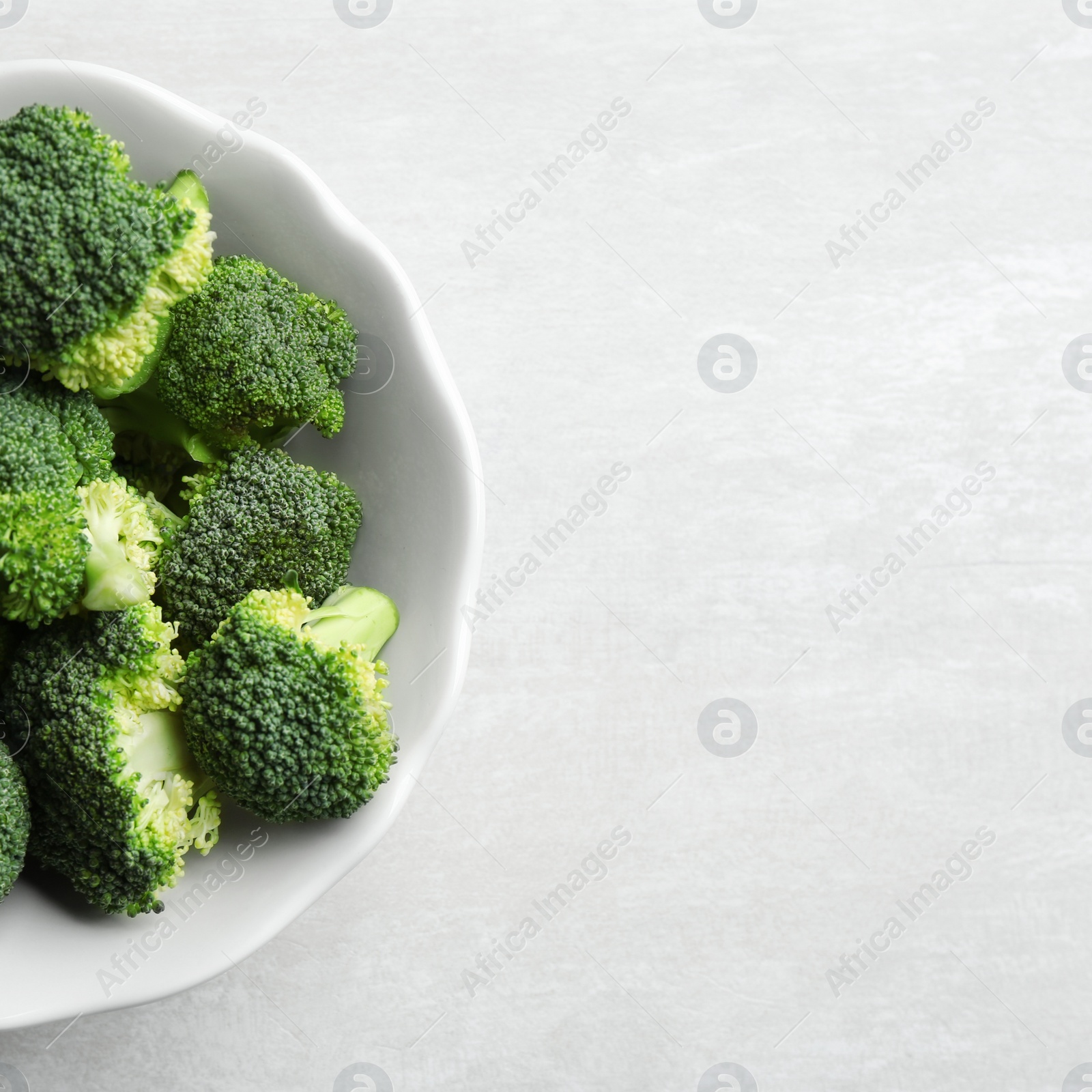 Photo of Bowl of fresh broccoli on light grey table, top view with space for text