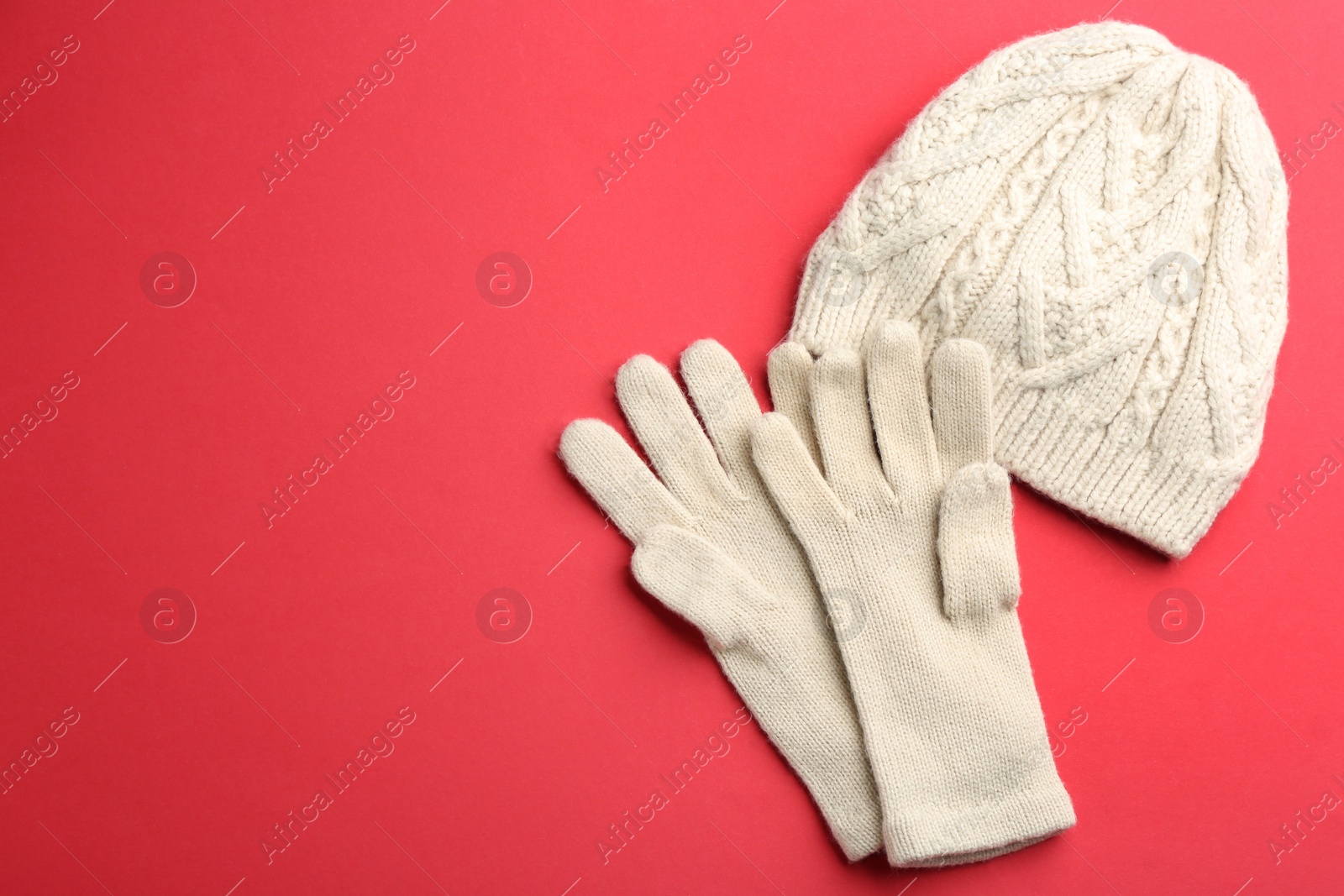 Photo of Woolen gloves and hat on red background, flat lay. Space for text