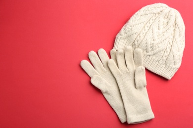 Woolen gloves and hat on red background, flat lay. Space for text