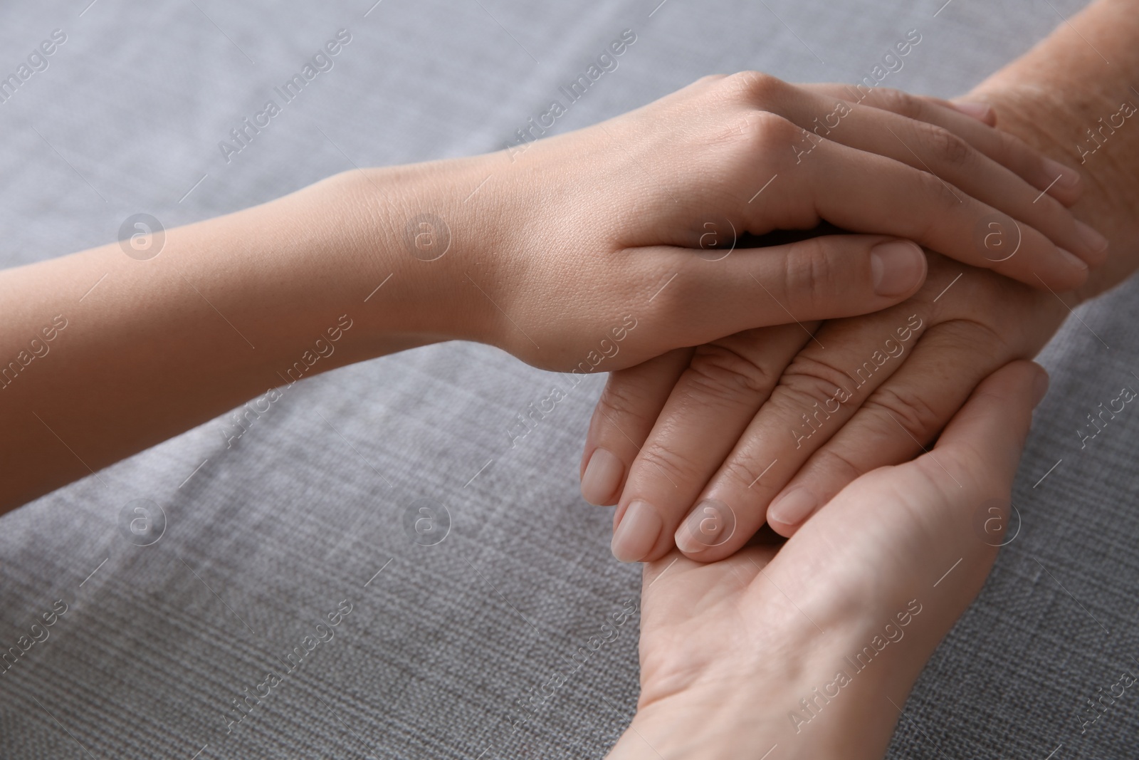 Photo of Young and elderly women holding hands together on grey fabric, closeup