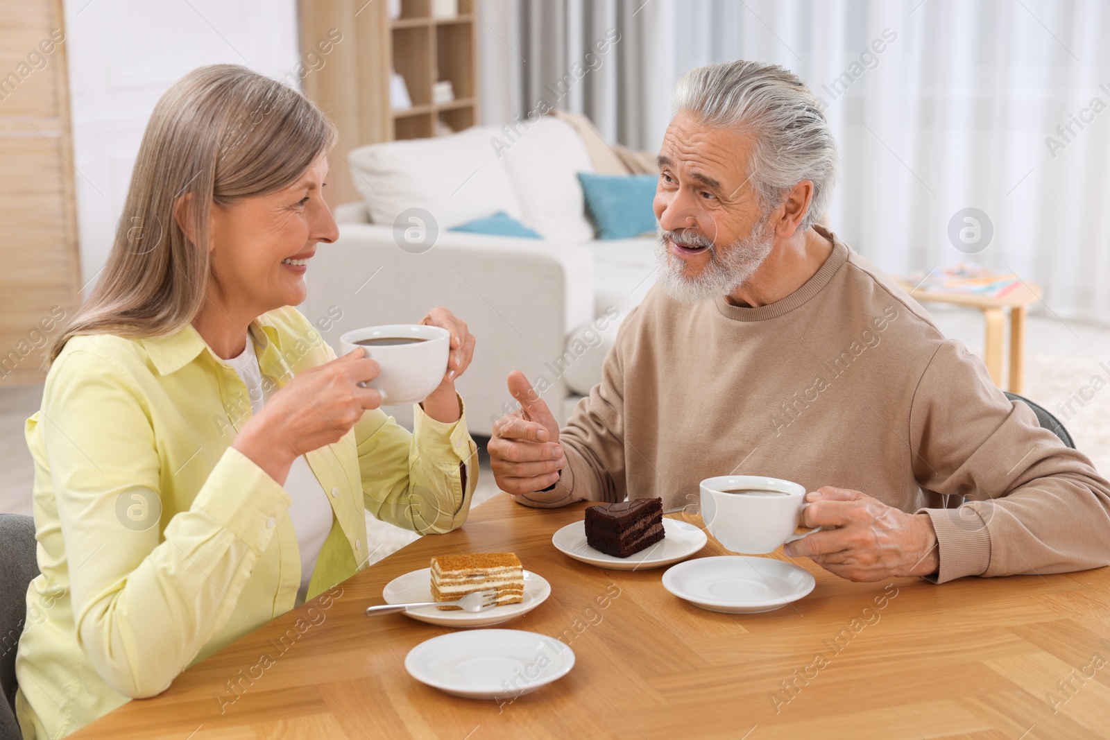 Photo of Affectionate senior couple having breakfast at wooden table in room