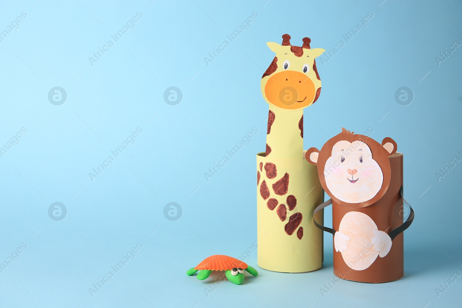 Photo of Toy monkey and giraffe made from toilet paper hubs with plasticine turtle on light blue background, space for text. Children's handmade ideas